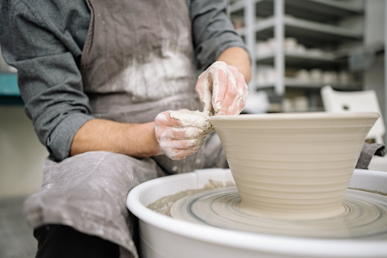 Artisan shaping clay on a potter's wheel in a workshop, showcasing skill and craftsmanship.